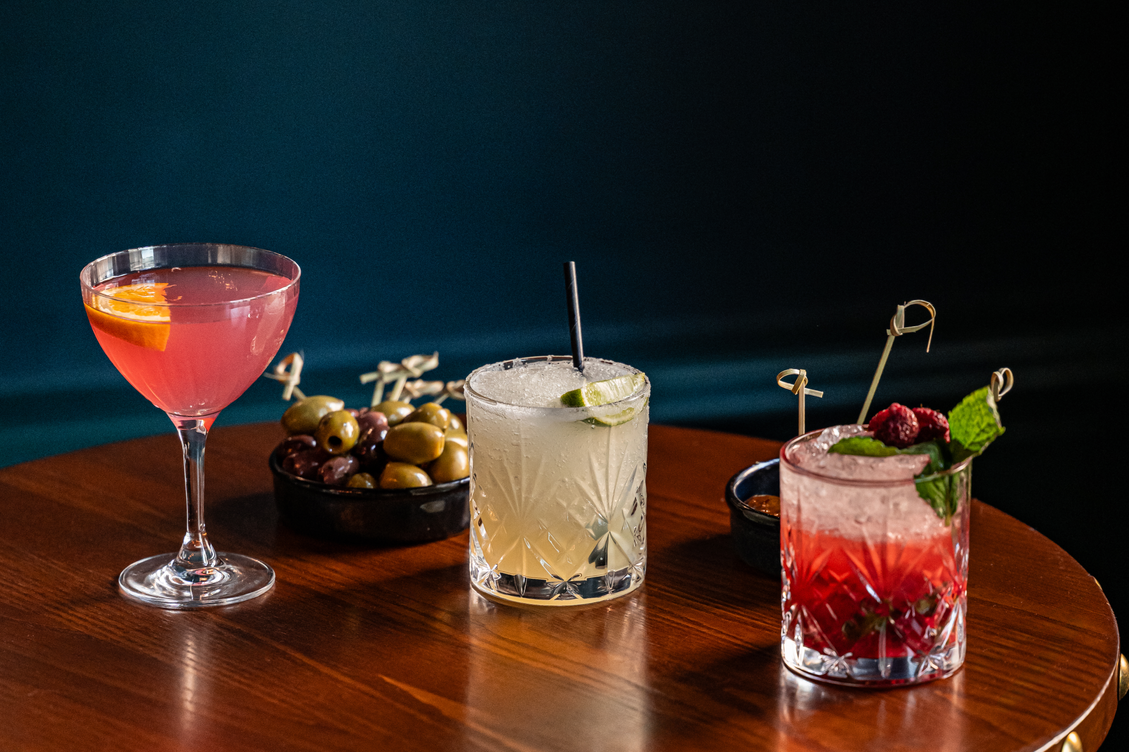 three cocktails lined up with nibbles